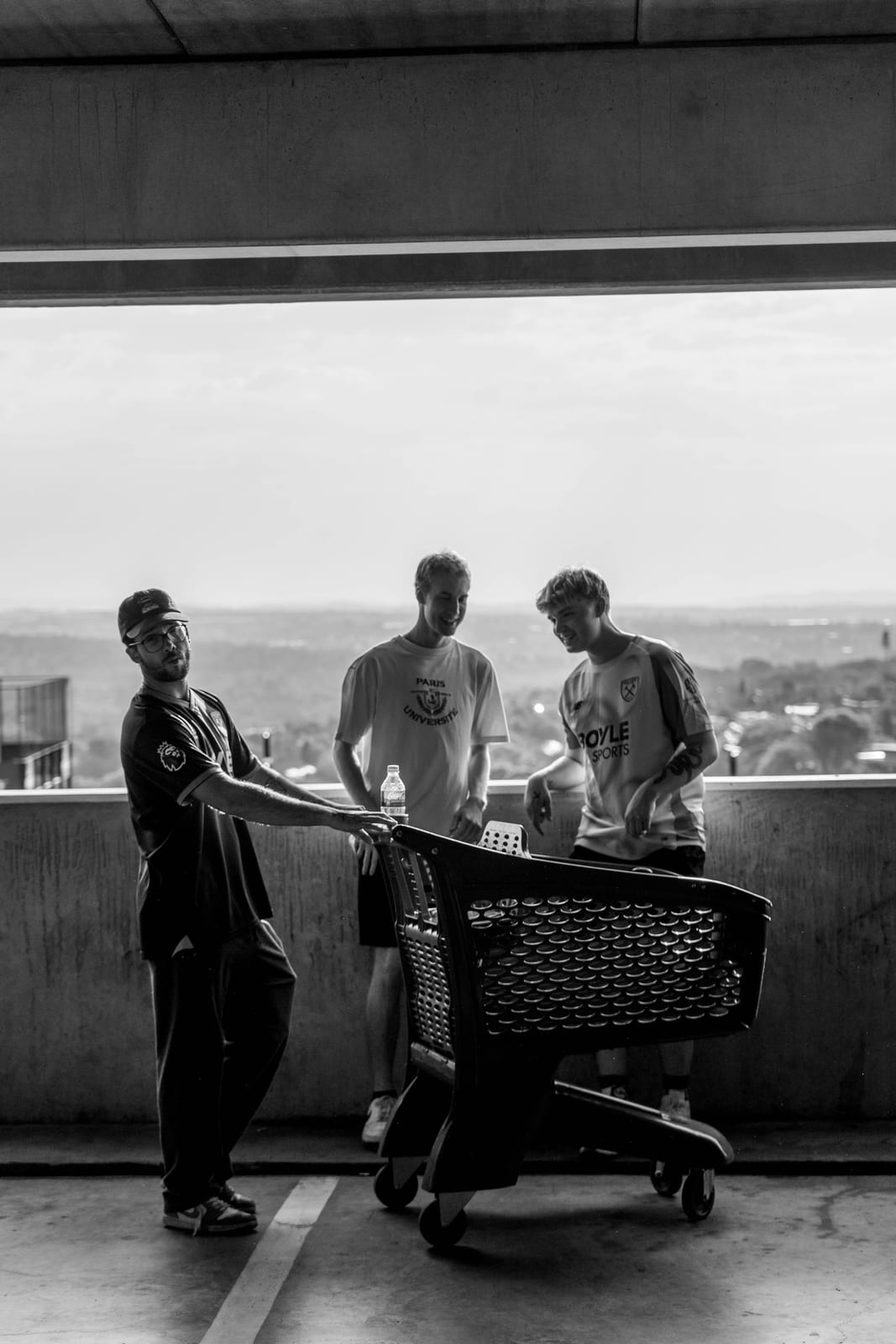 Black and white: three friends with a shopping trolley on the top deck of a parkade