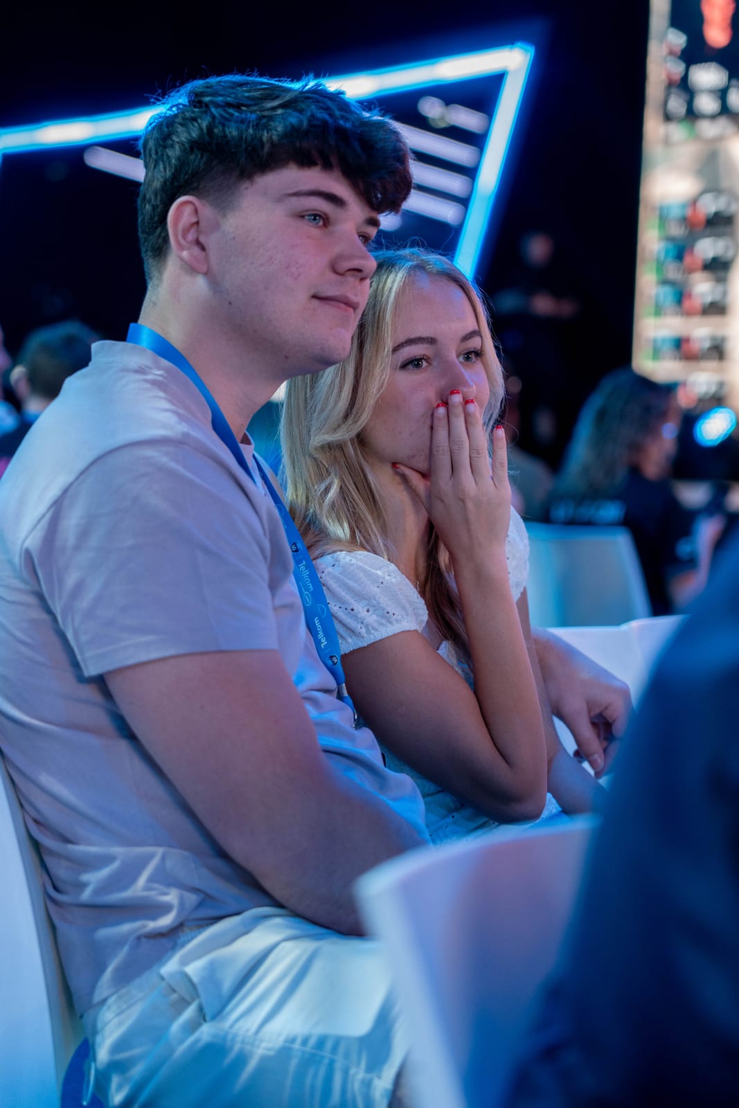 Two people in a crowd reacting, lit blue by the stage