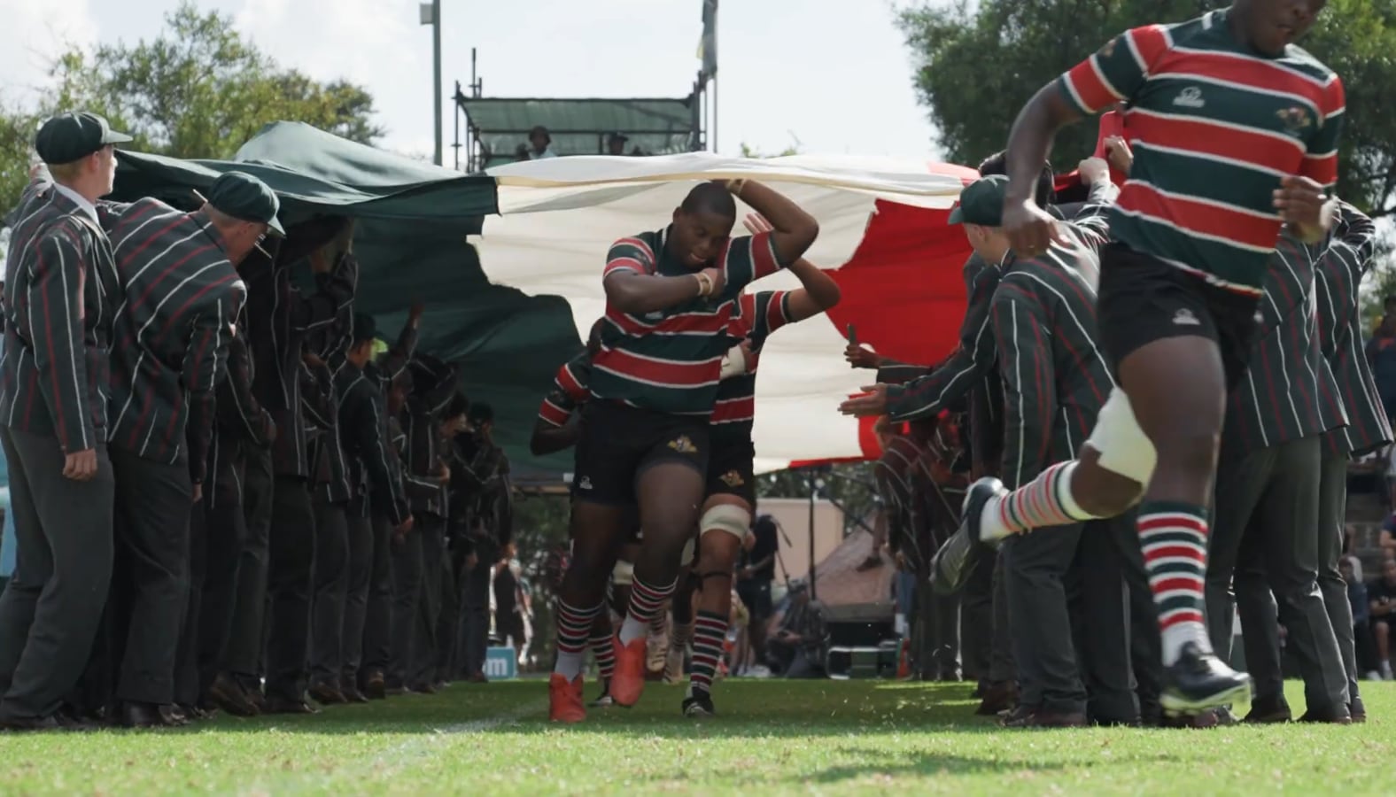 Still from Rugby Festival: a rugby team running out through a tunnel of schoolboys