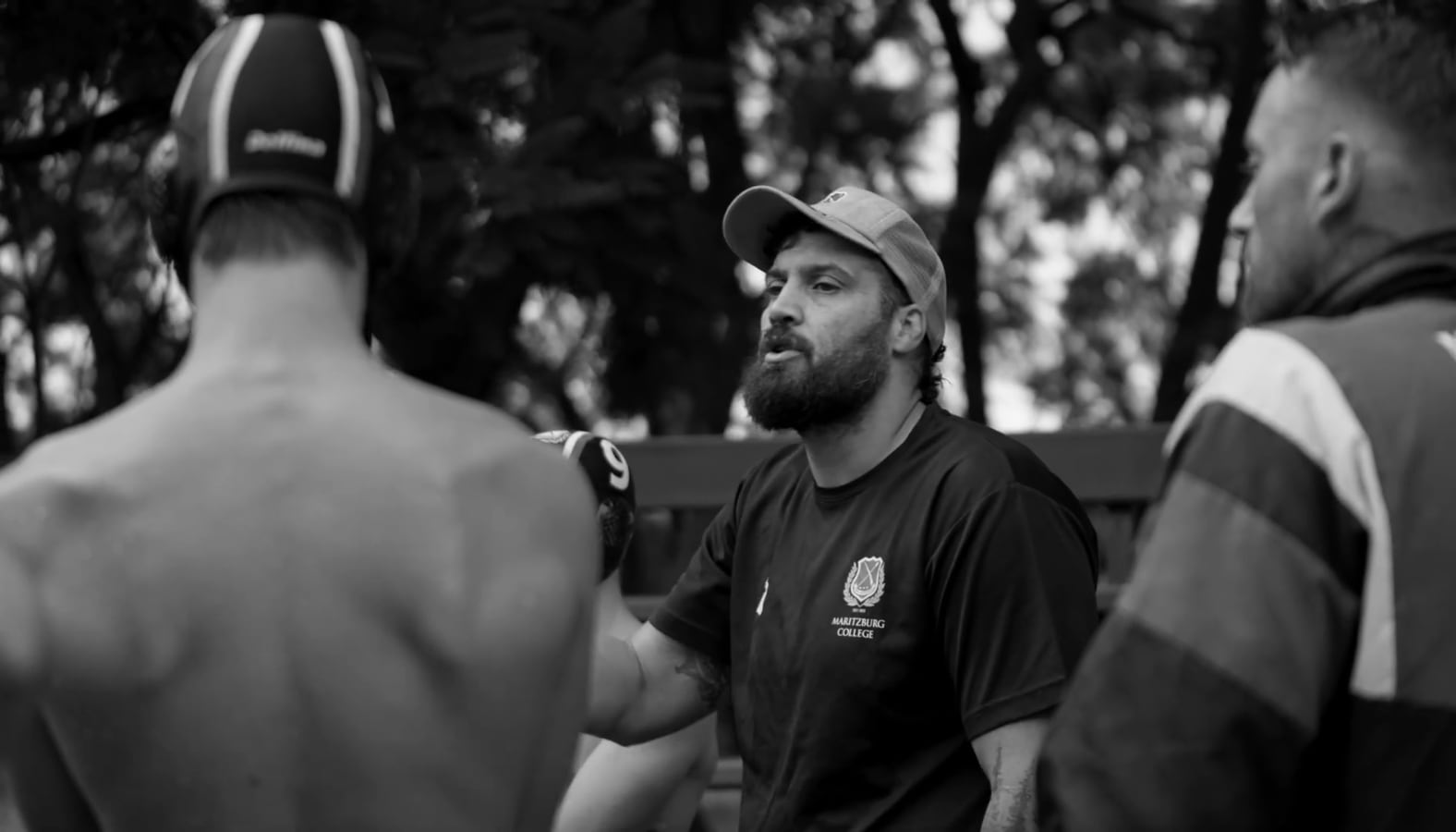 Still from Water Polo, in black and white: a coach talking to players in a huddle